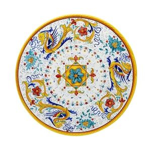 May include: Circular ceramic table top, hand-painted with a white base. It showcases blue, yellow, and red floral and mythical creature patterns. The edge is finished with a yellow rope-style border.