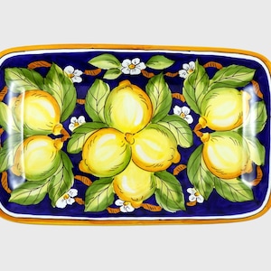 Può includere: Un piatto da portata rettangolare in ceramica con sfondo blu e un disegno dipinto a mano di limoni, foglie e fiori bianchi. Il piatto ha un bordo giallo.