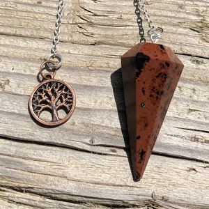 May include: A brown and black speckled crystal pendulum with a silver chain and a copper tree of life charm.