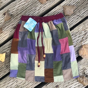 May include: A patchwork corduroy skirt with a burgundy waistband and drawstring. The skirt is made of different colored squares of corduroy, including green, brown, purple, and beige. The skirt has a tag that says "wearing".
