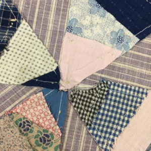 May include: A close-up of a patchwork quilt featuring a range of fabrics in shades of blue, pink, white, and black. The quilt is composed of small squares and triangles, with visible seams. The quilt is crafted from a variety of fabrics, including gingham, floral prints, and plain colours.