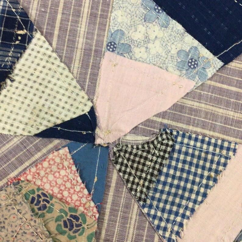 May include: A close-up of a patchwork quilt featuring a range of fabrics in shades of blue, pink, white, and black. The quilt is composed of small squares and triangles, with visible seams. The quilt is crafted from a variety of fabrics, including gingham, floral prints, and plain colours.