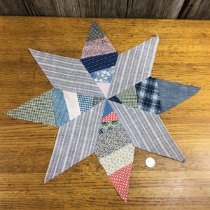 May include: A patchwork quilt block in the shape of a star with a variety of blue, pink, red, and white fabrics. The star is made up of smaller triangles and squares.