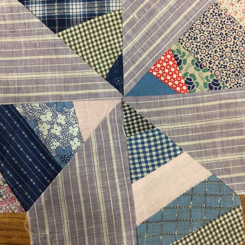 May include: A close-up of a quilt made from various fabrics in shades of blue, pink, white and black. The quilt is made of squares and triangles, and the fabrics are patterned with stripes, gingham and floral designs.