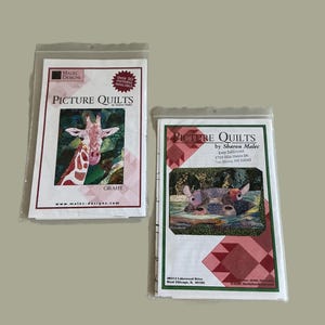 May include: Two packaged picture quilt patterns. One features a giraffe with the word "GIRAFFE" below. The other shows a quilt with three animals in a pond. Both packages have the text "PICTURE QUILTS" and the designer's name.