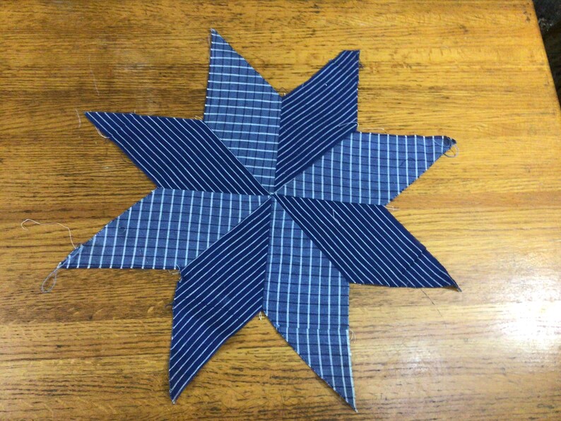 May include: A blue and white striped fabric star with eight points. The star is made of two different fabrics, one with a white and blue plaid pattern and the other with a white and blue striped pattern.