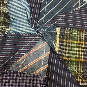May include: A close-up of a patchwork quilt made from different fabrics. The quilt is made of various shades of blue, brown, and green fabrics with white stitching. The fabrics are arranged in a star pattern.
