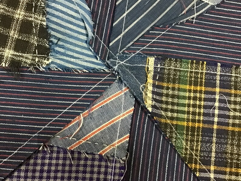 May include: A close-up of a patchwork quilt made from different fabrics. The quilt is made of various shades of blue, brown, and green fabrics with white stitching. The fabrics are arranged in a star pattern.