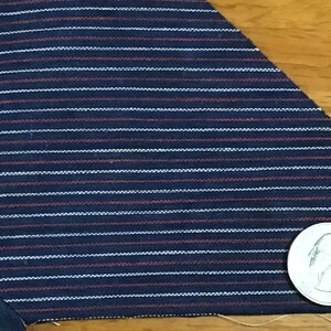 May include: Close-up of a dark blue fabric with thin white and red stripes. A silver coin is visible in the bottom right corner of the image.