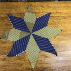 May include: A handmade patchwork star quilt block with a blue and yellow plaid pattern. The block is made of eight triangles, each with a different pattern. The block is a traditional quilt pattern.