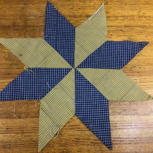 May include: A blue and yellow patchwork star made from fabric with a checkered pattern. The star is made of eight points and is a traditional quilt block.