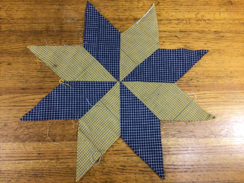 May include: A blue and yellow patchwork star made from fabric with a checkered pattern. The star is made of eight points and is a traditional quilt block.