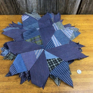 May include: A blue and white patchwork quilt block in the shape of a star. The block is made of various shades of blue and white striped fabric.
