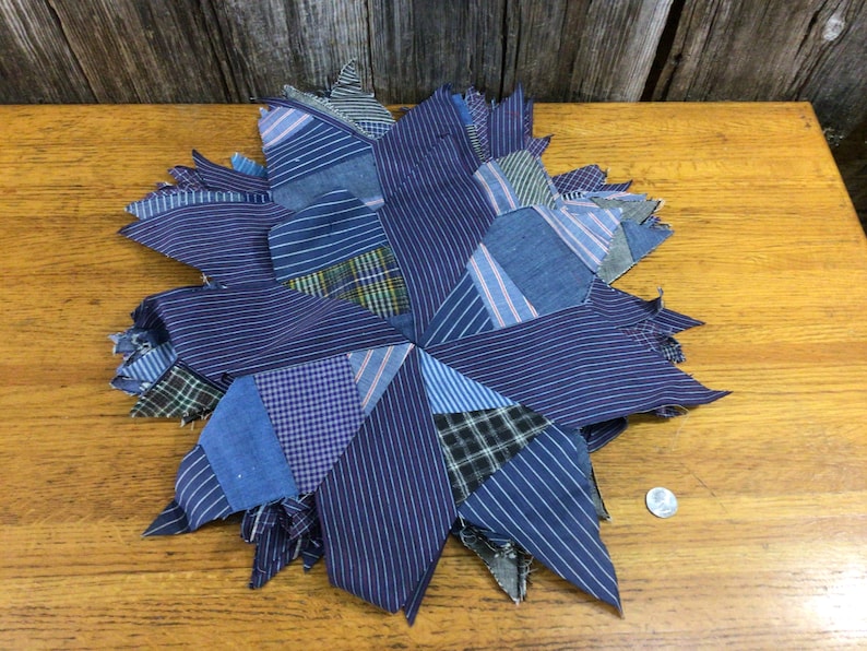 May include: A blue and white patchwork quilt block in the shape of a star. The block is made of various shades of blue and white striped fabric.