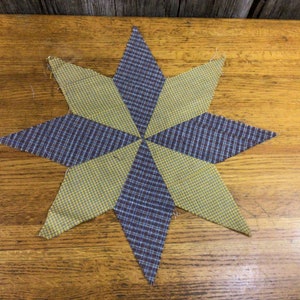 May include: A yellow and blue plaid fabric star, with a geometric design, is displayed on a wooden surface.