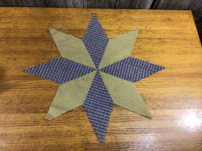 May include: A yellow and blue plaid fabric star, with a geometric design, is displayed on a wooden surface.