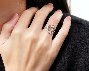 May include: A silver ring with a tree of life design. The ring is worn on a person's finger.
