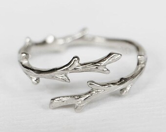 May include: A silver ring with a delicate design of intertwined branches. The branches have small, detailed leaves.