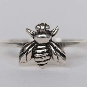 Può includere: Un anello d'argento con un designo di ape dettagliato. L'ape è rivolta in avanti con le ali spiegate.