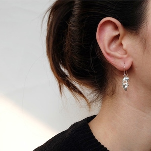 May include: Silver dangle earrings featuring a face-shaped design. The earrings are made of a smooth, shiny metal and have a simple, elegant style.