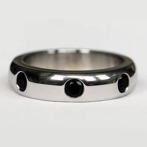 May include: A silver-colored ring with three black gemstones evenly spaced around the band. The ring has a smooth, polished finish and a rounded shape, creating a modern and minimalist aesthetic.