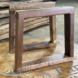 Könnte beinhalten: Zwei Tischbeine aus Holz mit rechteckigem Rahmendesign. Die Beine bestehen aus dunkelbraunem Holz mit sichtbarer Maserung und natürlicher Oberfläche. Die Beine sind robust und für einen Tisch oder andere Möbel geeignet.