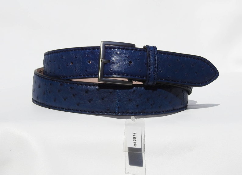 May include: A dark blue leather belt with a silver buckle and an ostrich skin pattern. The belt is rolled up and has a tag attached that says "cod. 2087-6".