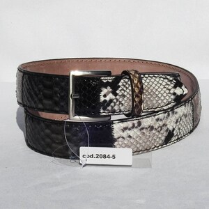 May include: A black and white snakeskin belt with a silver buckle. The belt is rolled up and has a tag that says "cod.2084-5".