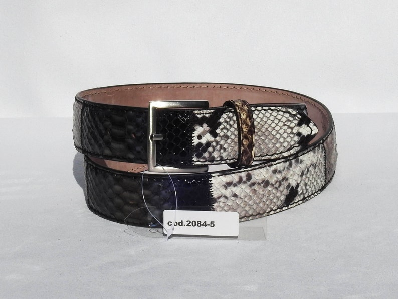 May include: A black and white snakeskin belt with a silver buckle. The belt is rolled up and has a tag that says "cod.2084-5".