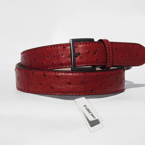 May include: A red leather belt with an ostrich skin pattern and a silver buckle. The belt is folded in half and the tag reads "Cod. 2087-S".