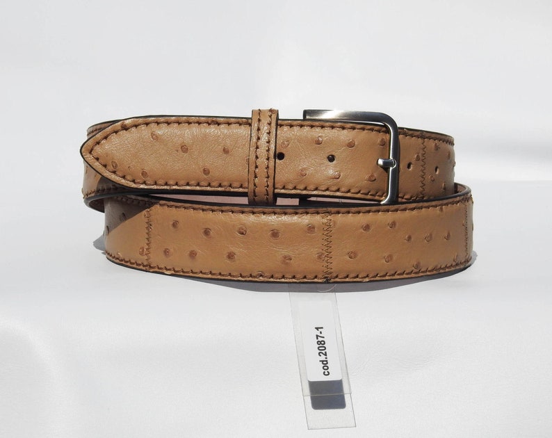 May include: A tan leather belt with an ostrich skin pattern and a silver buckle. The belt is folded in half and the tag reads "cod.2087-1".