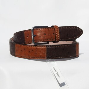 May include: A brown and black leather belt with an ostrich skin pattern. The belt has a silver buckle and is stitched with brown thread. The tag attached to the belt reads "cod.2087-2".