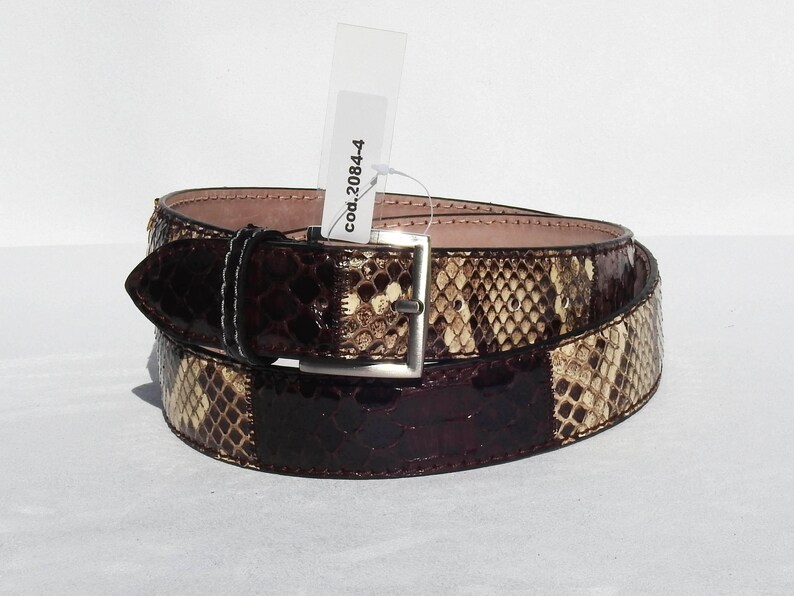 May include: A brown and beige snakeskin belt with a silver buckle. The tag attached to the belt reads "cod.20844".