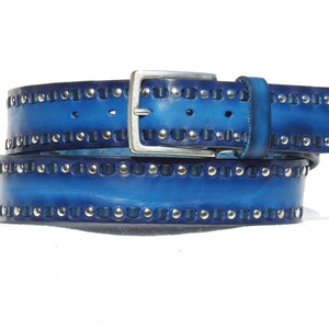 Puede incluir: Un cinturón de cuero azul con tachuelas plateadas y una hebilla plateada. El cinturón está doblado por la mitad y la hebilla es visible.