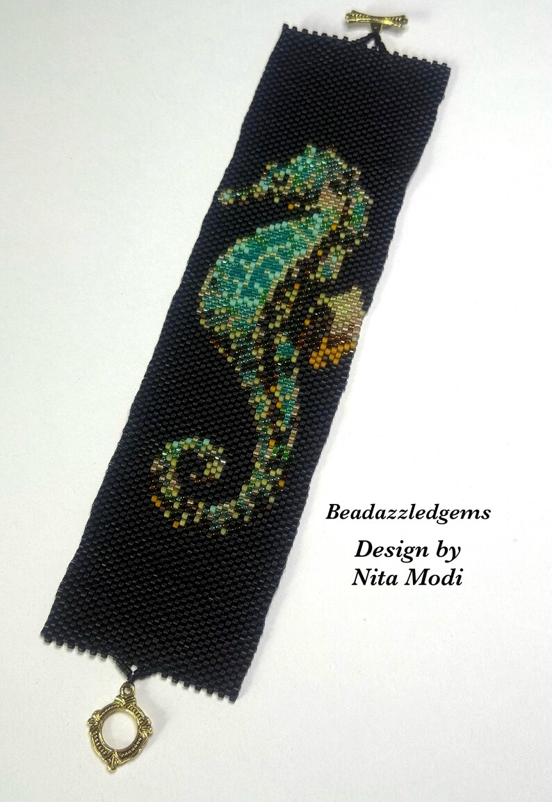 May include: Black beaded bracelet featuring a seahorse design in shades of teal, green, and gold. The bracelet has a decorative clasp and the text "Beadazzledgems Design by Nita Modi".