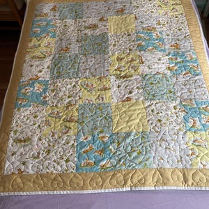 May include: A patchwork quilt with a cream background and a variety of floral patterns in shades of blue, yellow, and green. The quilt is edged with a tan border and has a heart-shaped quilting pattern.