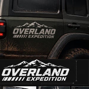 Può includere: Un adesivo in vinile bianco con una grafica di una catena montuosa sopra il testo OVERLAND EXPEDITION. Il design include una serie di linee diagonali. L'adesivo è mostrato applicato sui pannelli laterali e posteriori di vari veicoli fuoristrada.