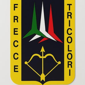 Op de afbeelding: Een geel, schildvormig embleem met de woorden "FRECCE" en "TRICOLORI" in verticale tekst. Het embleem heeft een donkerblauwe achtergrond met drie gestileerde pijlen in groen, wit en rood, en een gouden pijl en boog.