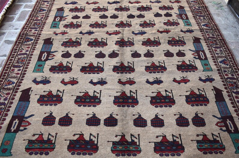 May include: A beige rug with a repeating pattern of stylized tanks and helicopters. The rug has a brown, red, and blue border.
