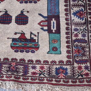 May include: A beige rug with a geometric pattern featuring stylized tanks and flowers. The rug has a red, blue, and green color scheme and a fringe border.
