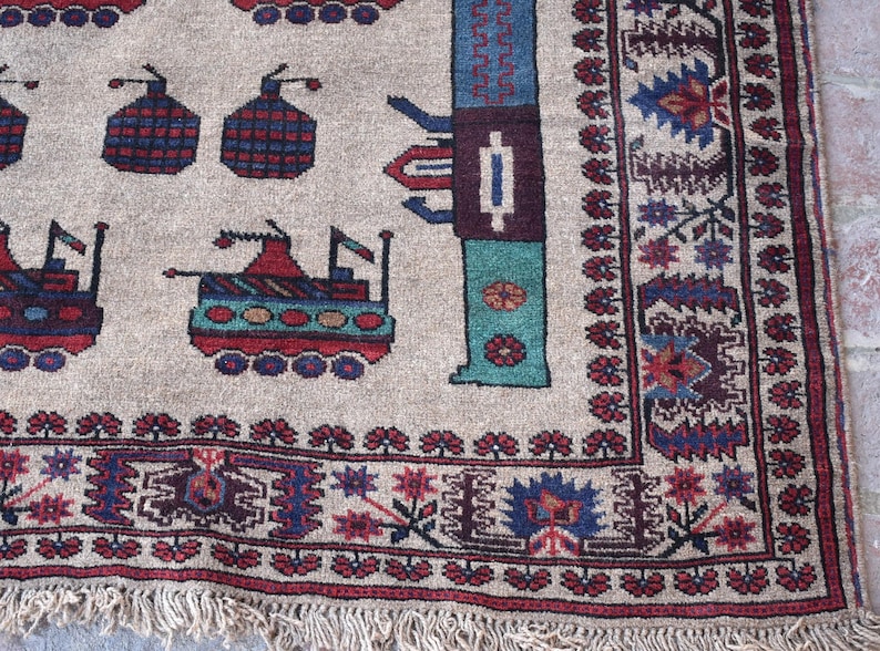 May include: A beige rug with a geometric pattern featuring stylized tanks and flowers. The rug has a red, blue, and green color scheme and a fringe border.