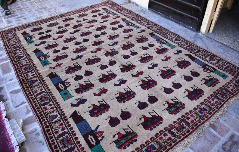 May include: A beige rug with a repeating pattern of stylized vehicles in shades of red, blue, and green. The rug has a border of intricate floral designs in shades of burgundy and white.
