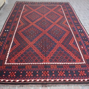 May include: A traditional red and blue rug with a geometric diamond pattern. The rug has a white border with a repeating design.