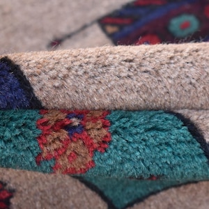 May include: Close-up of a beige rug with a colorful geometric pattern. The rug is folded in half, revealing the underside of the rug, which is also beige.