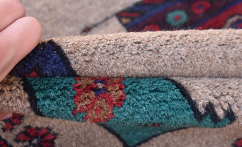 May include: Close-up of a beige rug with a colorful geometric pattern. The rug is folded in half, revealing the underside of the rug, which is also beige.