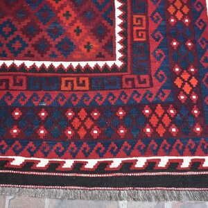 May include: Close-up of a red, blue, and white patterned rug with a fringe border. The rug has a traditional geometric design.