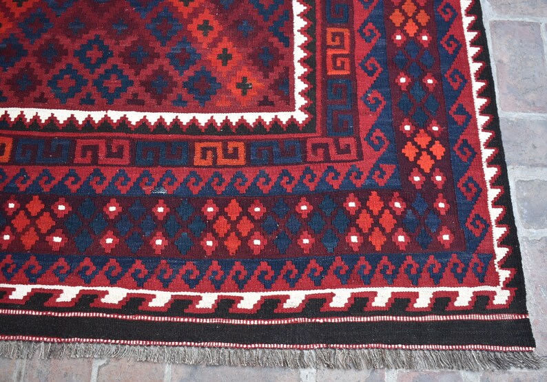 May include: Close-up of a red, blue, and white patterned rug with a fringe border. The rug has a traditional geometric design.