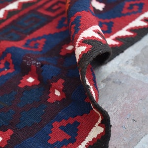 May include: Close-up of a red, blue, and white patterned rug with a geometric design. The rug is folded over and the edge is visible.