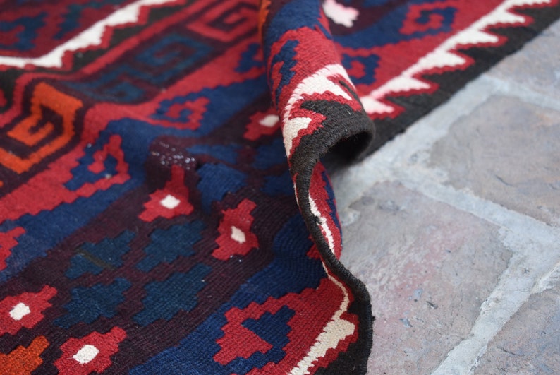 May include: Close-up of a red, blue, and white patterned rug with a geometric design. The rug is folded over and the edge is visible.