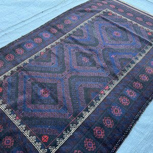 Pode incluir: Tapete retangular com um padrão geométrico azul escuro e bordô. O tapete apresenta um design central em losango com um padrão de borda repetitivo em bordô e branco. O tapete é feito de um material tecido.